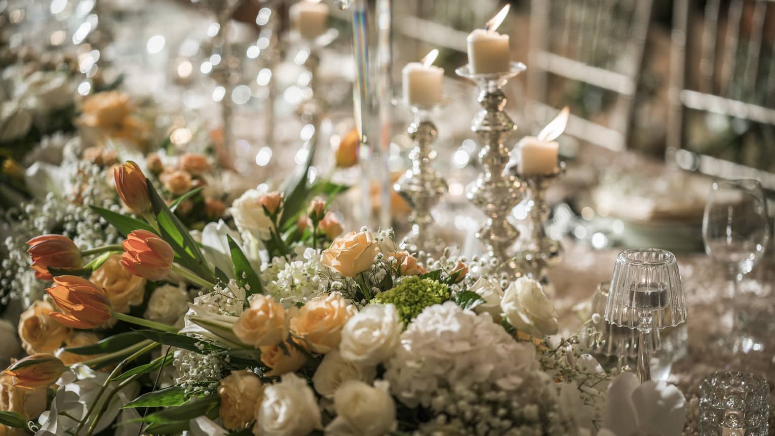 Close-up of flower arrangement with small white and peach roses, candles