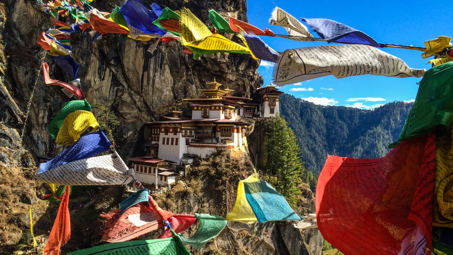 Colourful cloth blowing in the wind with a mountain monastery in the background.
