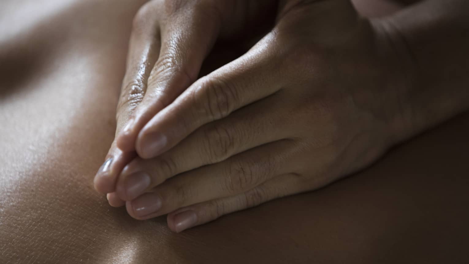 Two hands massage a person's back