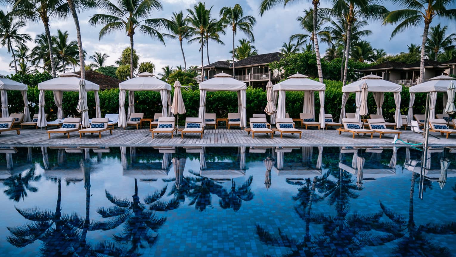 Pool reflecting palm trees, cabanas lined on pool deck