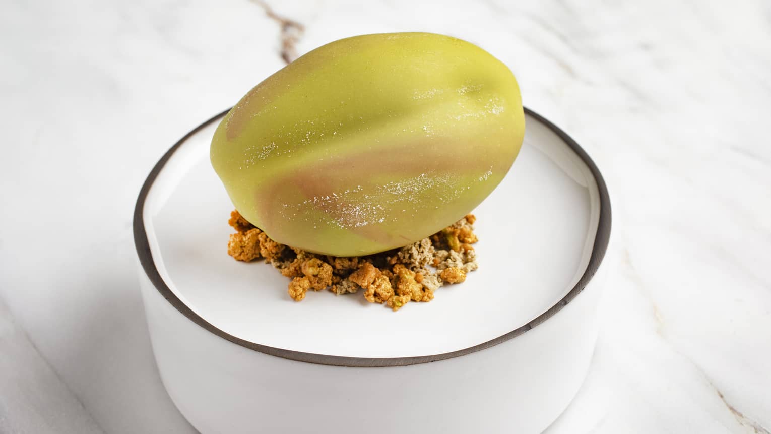 Sicilian pistachio cake placed atop pralines and cream and raspberry compote on a elevated round, white bowl