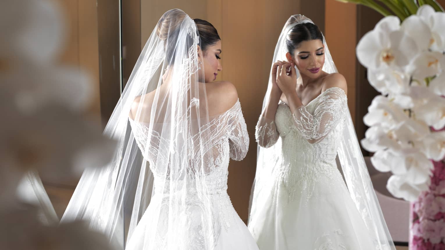 A bride in a white dress adjusting her earring in a mirror