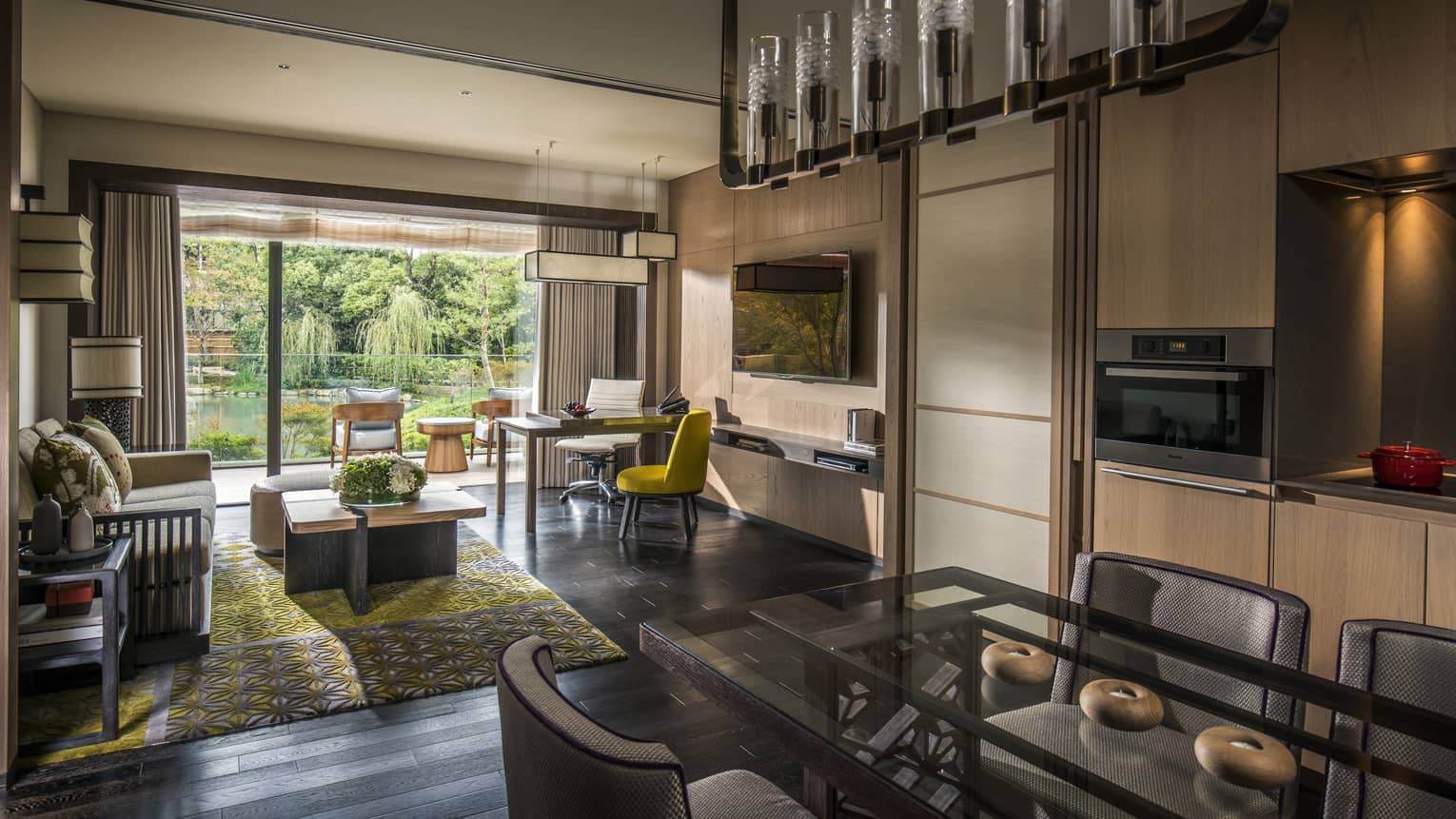 Long glass dining table under chandelier by living room, open wall to sunny patio