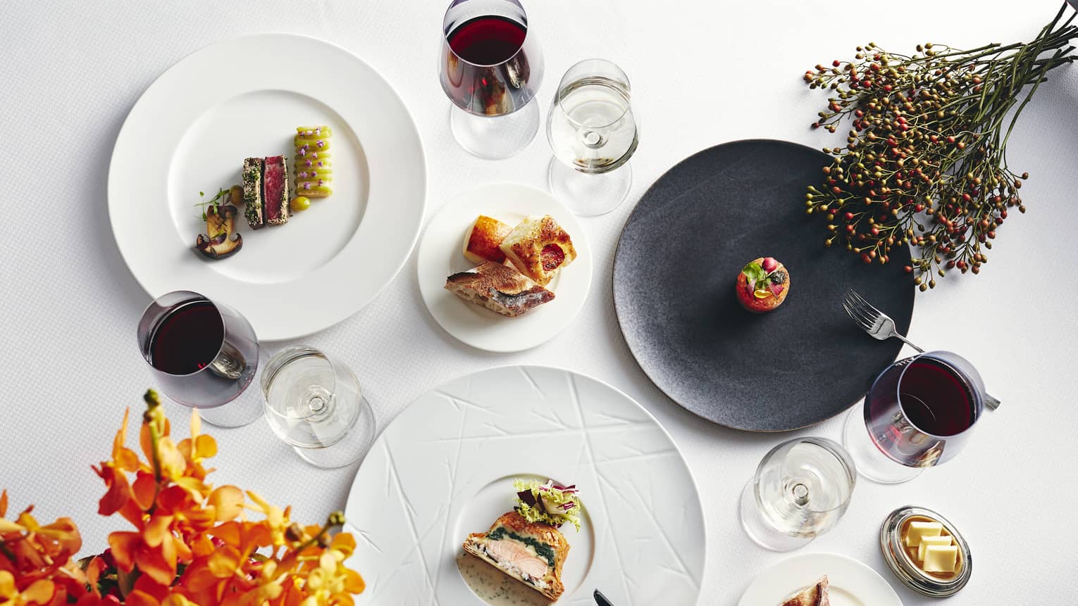 Autumn dining spread with salmon en croute, steak tartare, ceviche, bread & butter, glasses of wine and bouquets of flowers