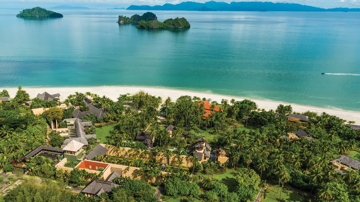 Aerial view over resort, tropical trees, white sand beach and ocean with large rock formations