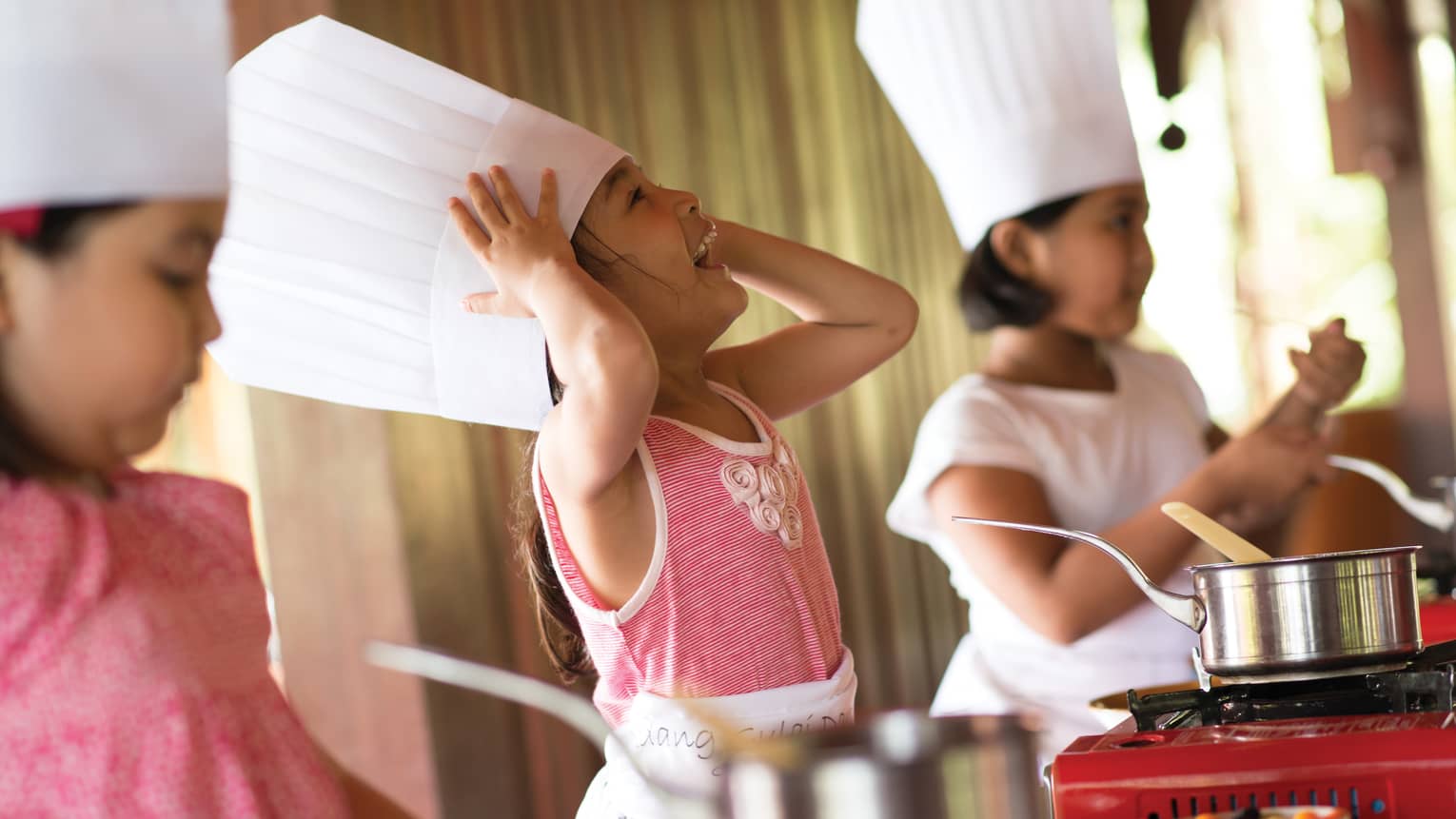 Three young children wearing tall white chef's hats in cooking class