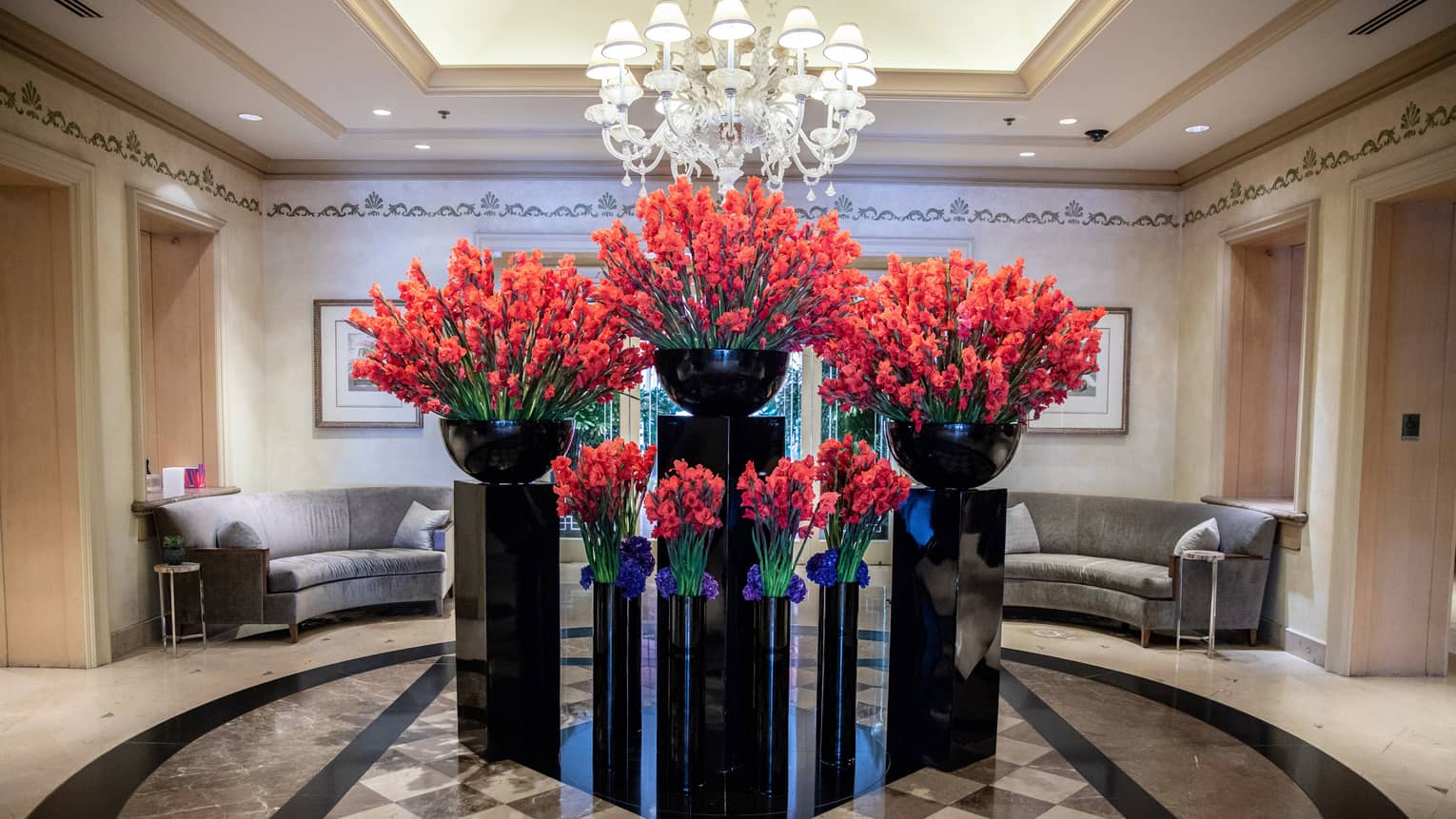 Hotel lobby, large red floral arrangements in black vases under crystal chandelier