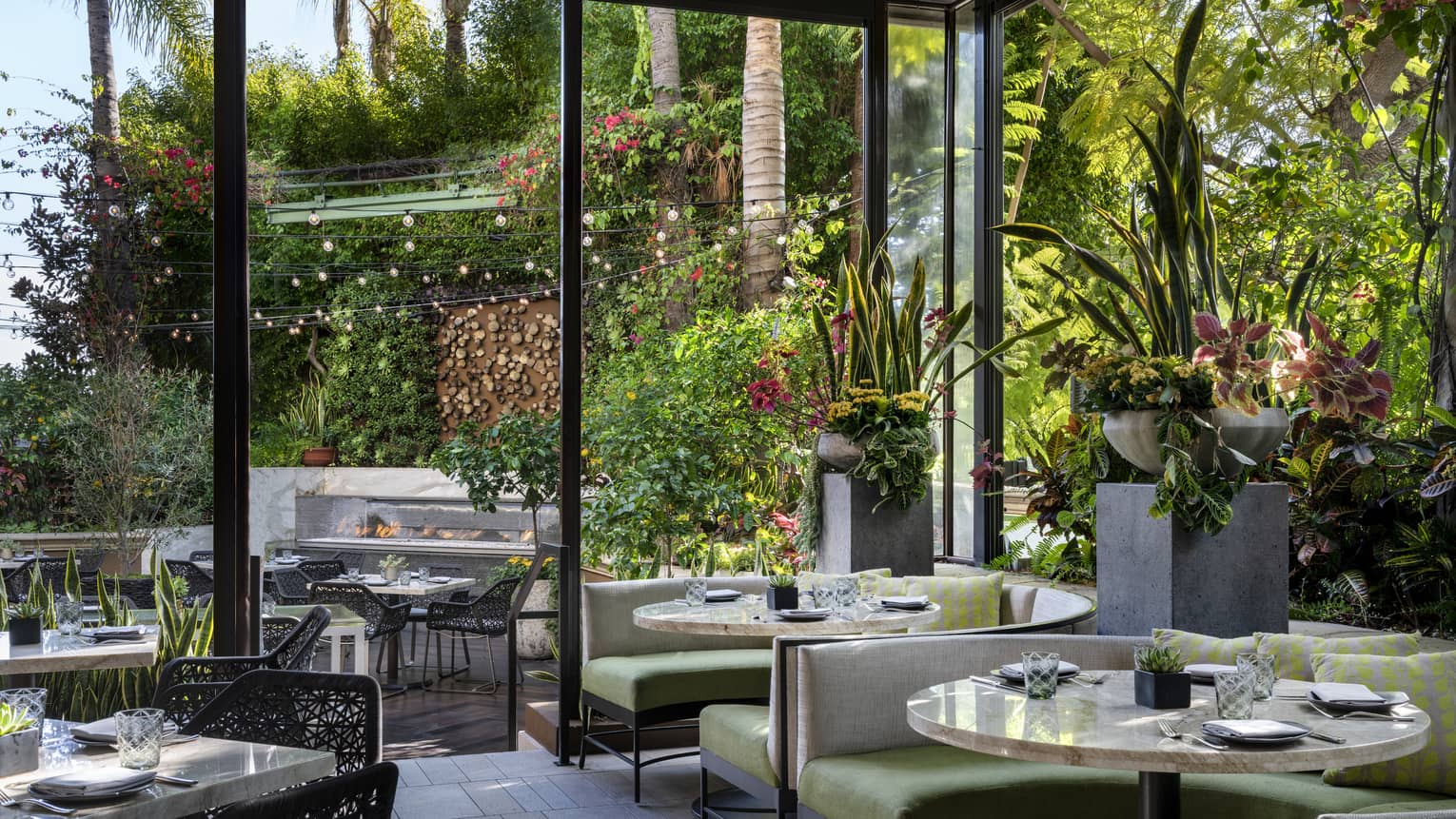 Restaurant seating with green chairs and many plants, with large windows leading to outdoor seating.