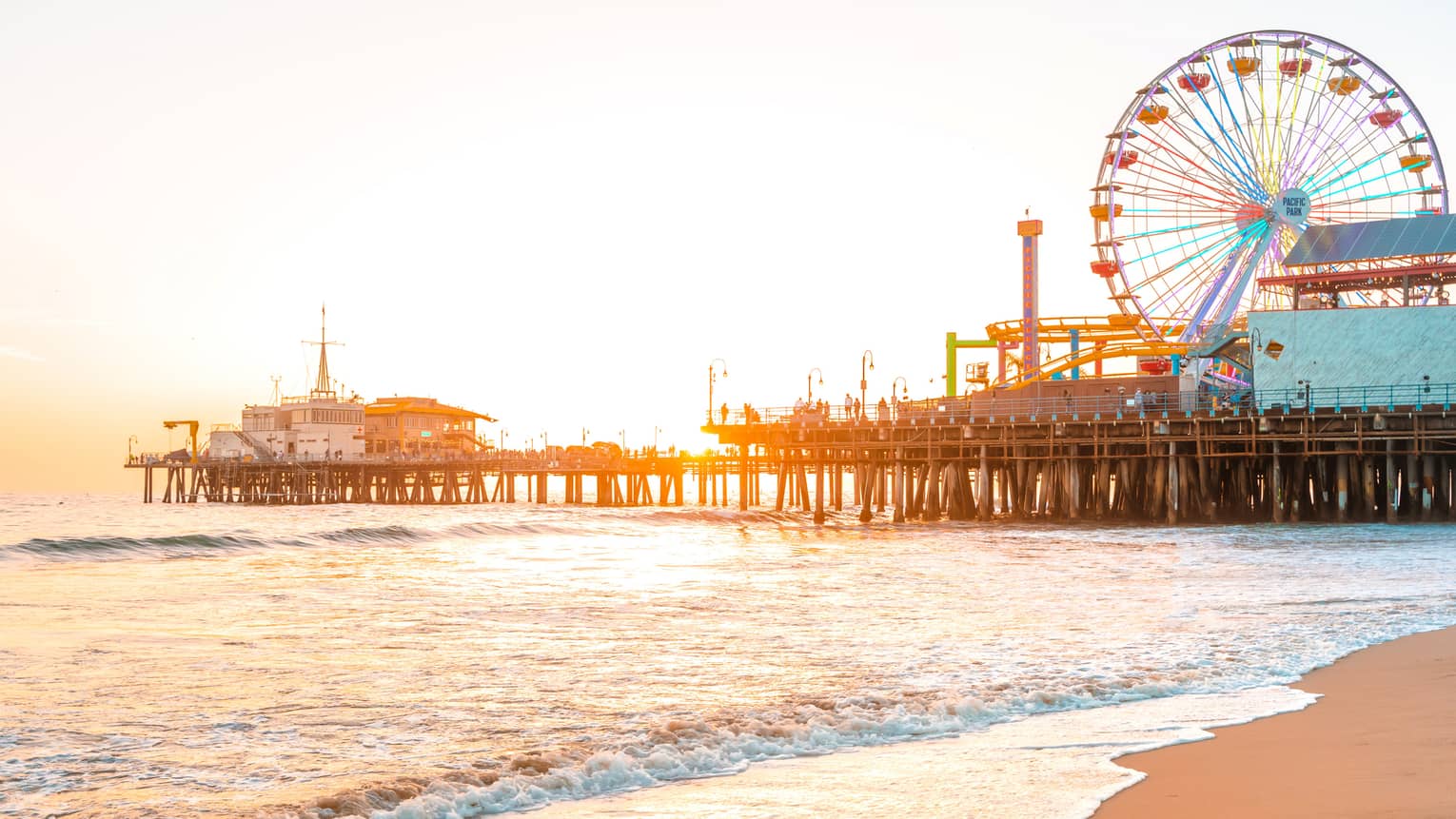 A pier on the beach with a ferris wheel at sunset