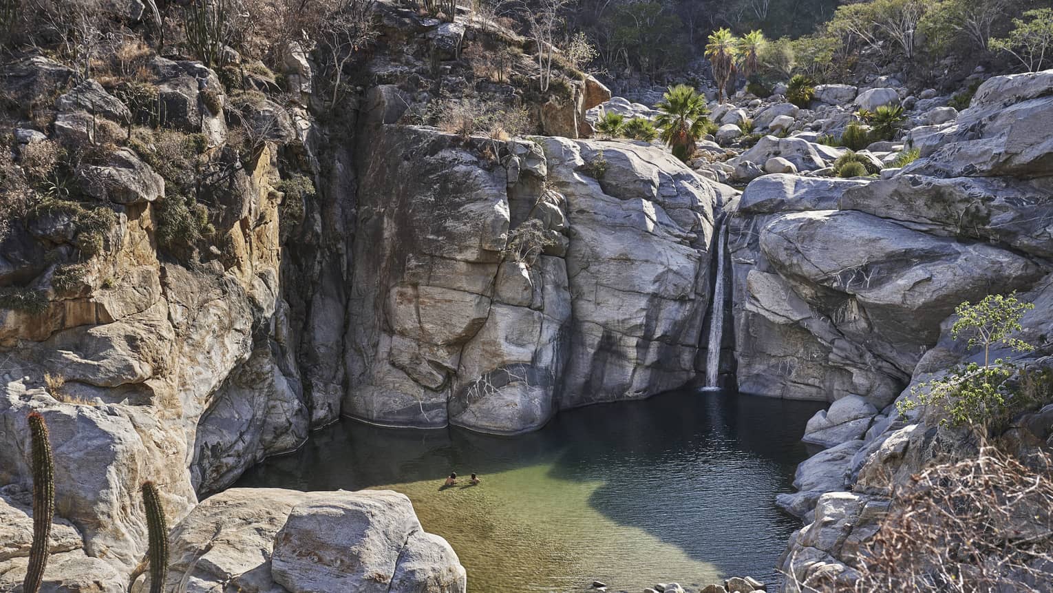 Two people wade in small ocean lagoon under large cliffs