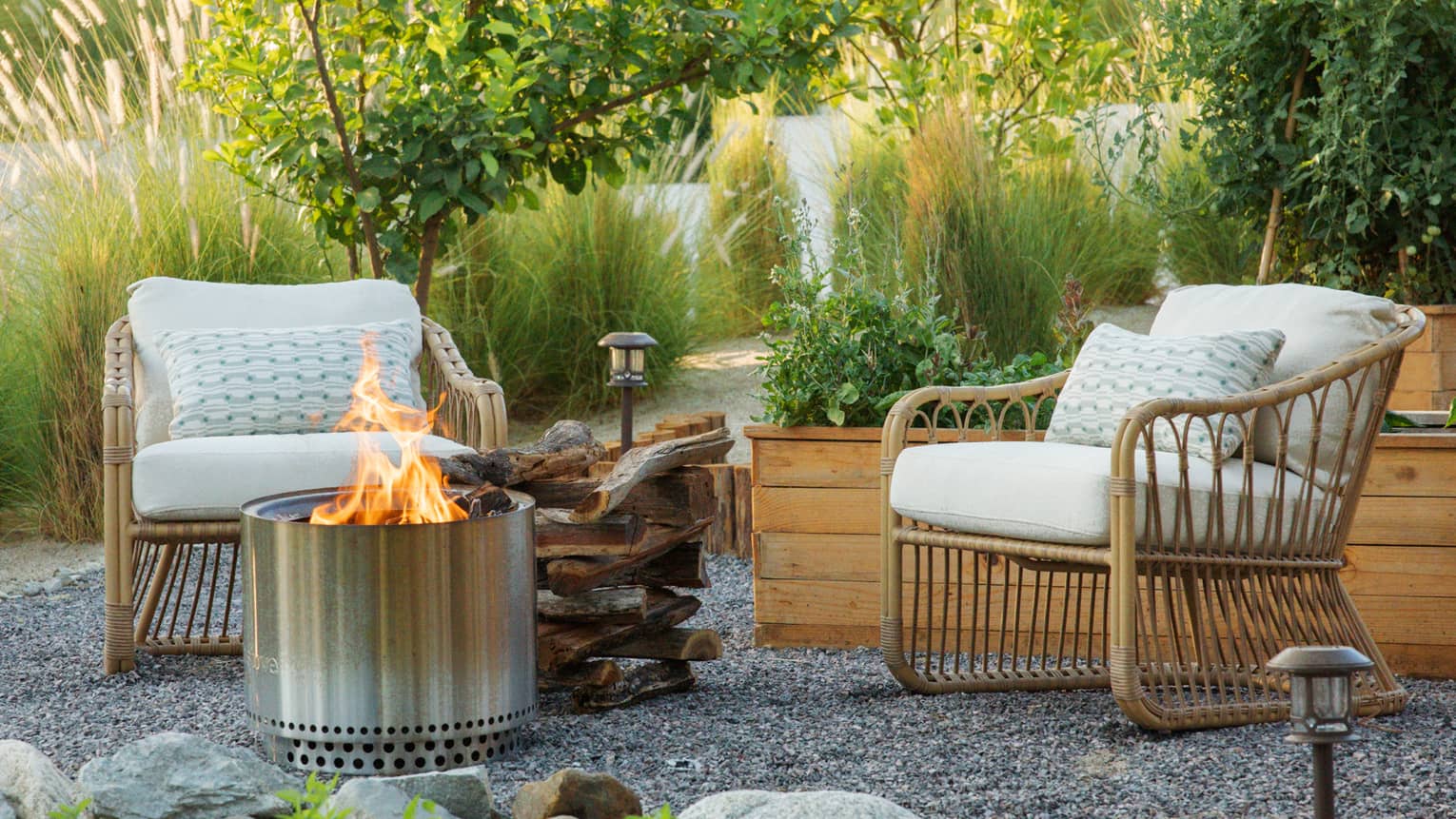 Two chairs beside a fire pit surrounded by plants and trees.