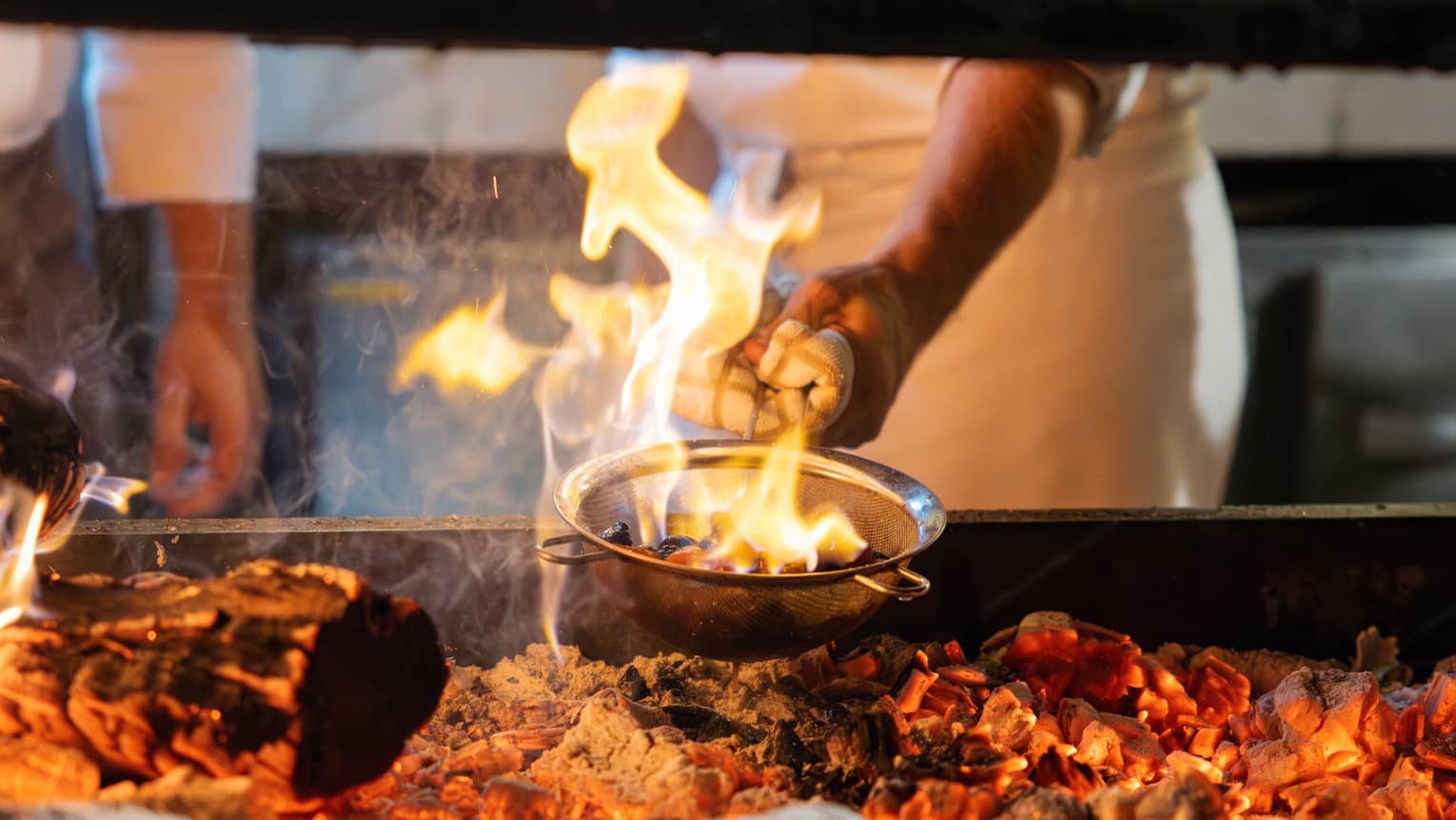 Chef cooking a dish over a fire grill.
