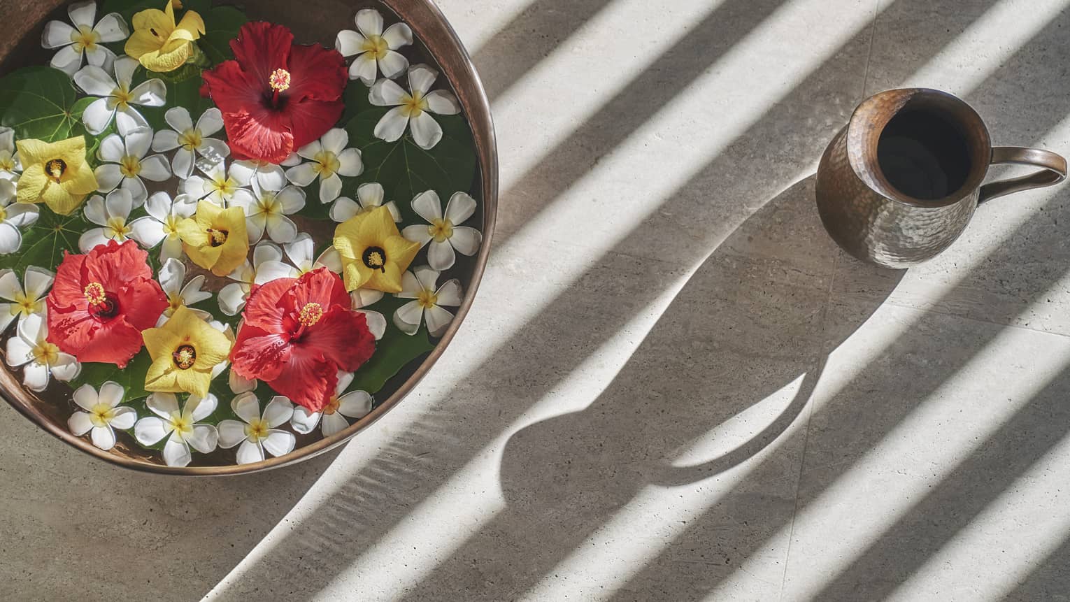 A bowl of flowers next to a cup.