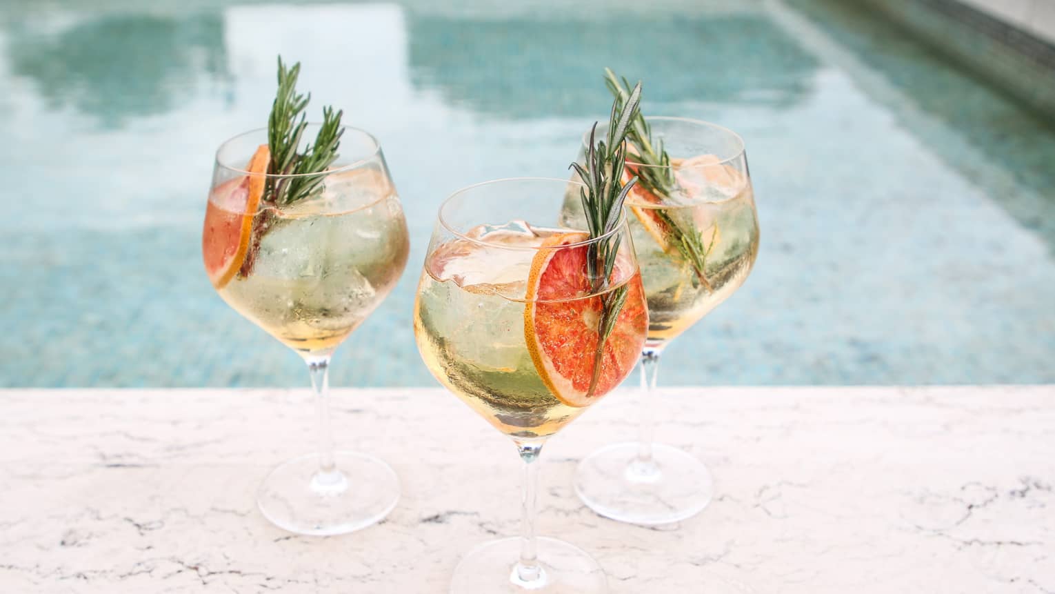 three white wine spritzers in crystal glasses, garnished with grapefruit slice and rosemary sprig