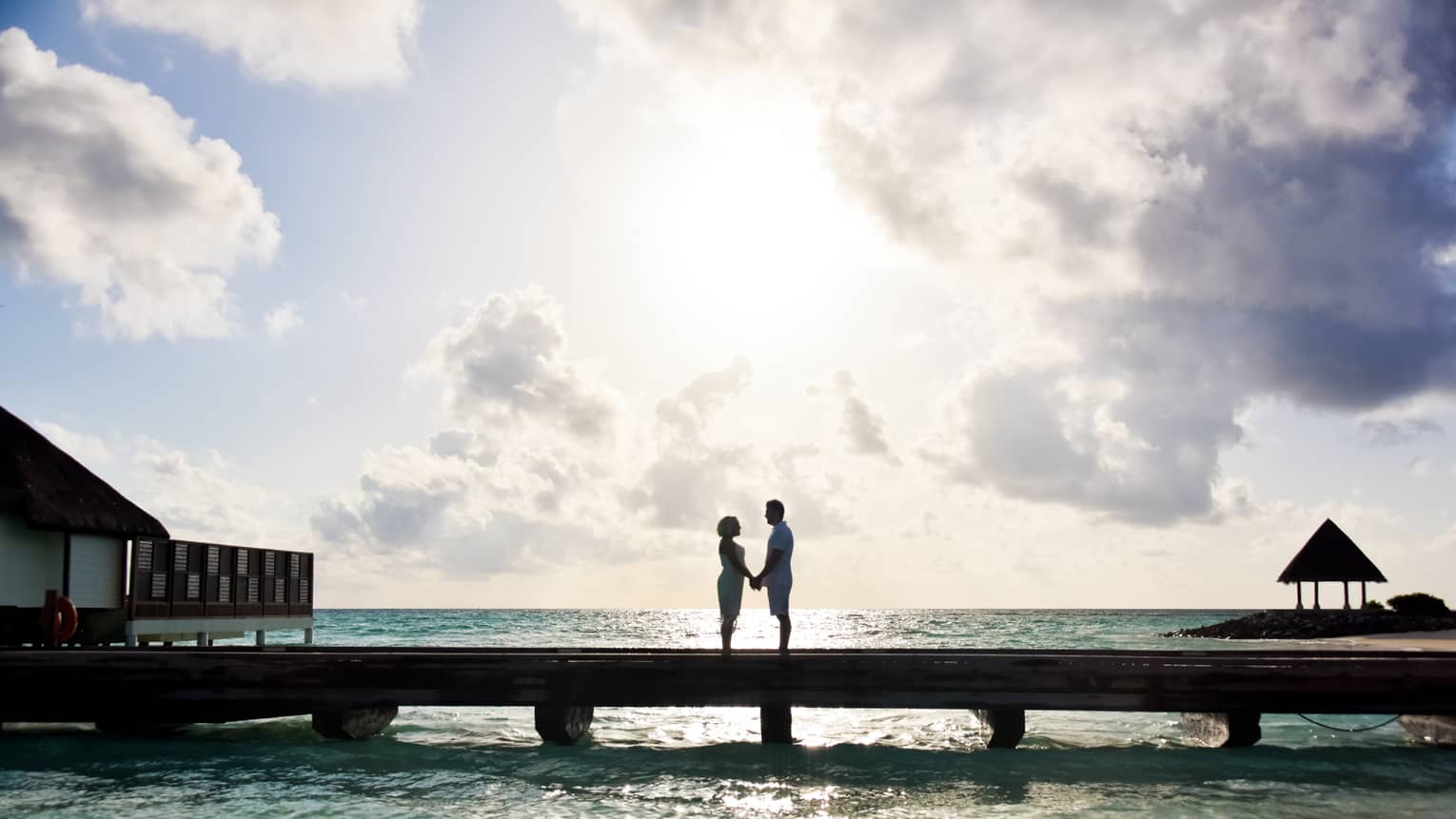 Couple holds hands, gaze at each other on long dock over lagoon