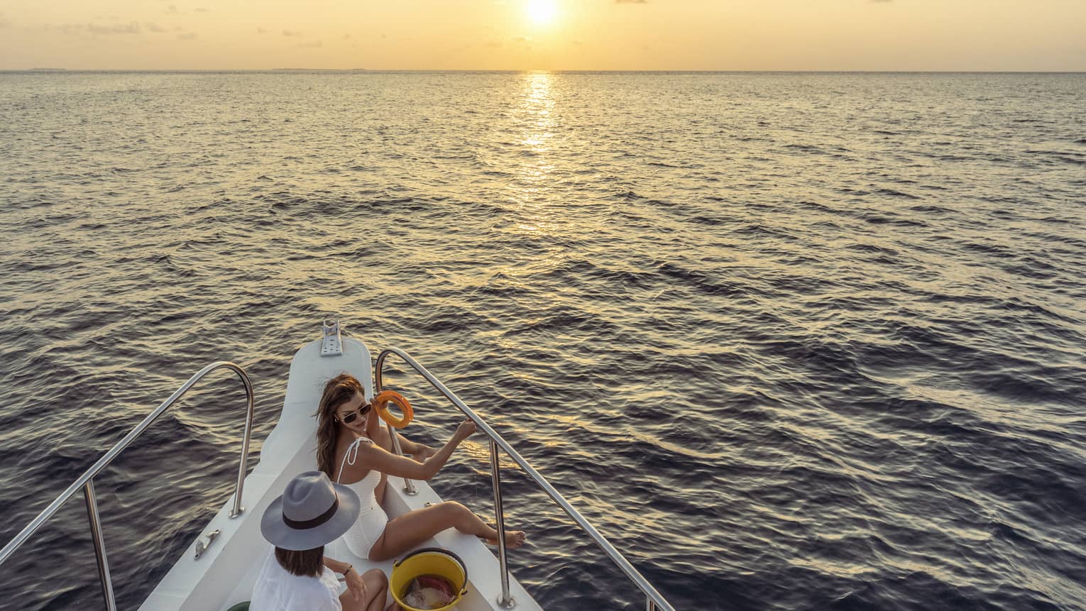 Two women enjoy snacks at the helm of a private yacht at sunset