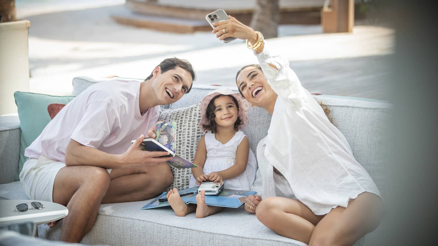 Smiling family of three takes a selfie on outdoor sofa