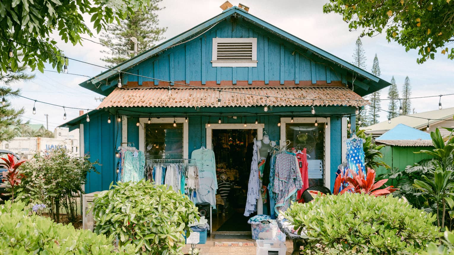 A shop in a small bright turquoise house surrounded by greenery