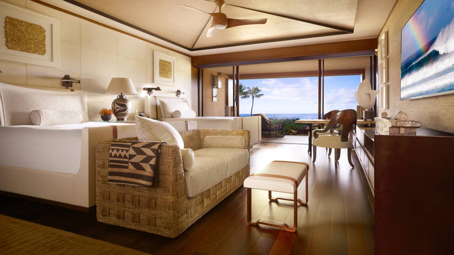 Oceanfront Room bed, wicker sofa with white cushions, bench at foot, dining table by open wall to patio