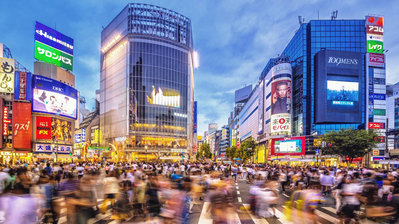 Image of blurry crowds along sidewalk under glass buildings, colourful billboards at night