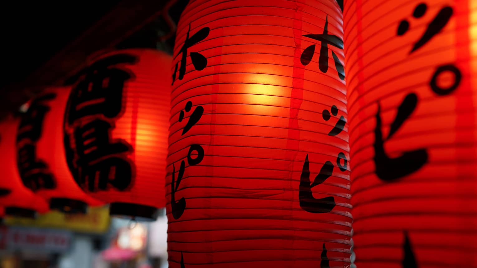 A close-up of illuminated red lanterns decorated with black Japanese writing 