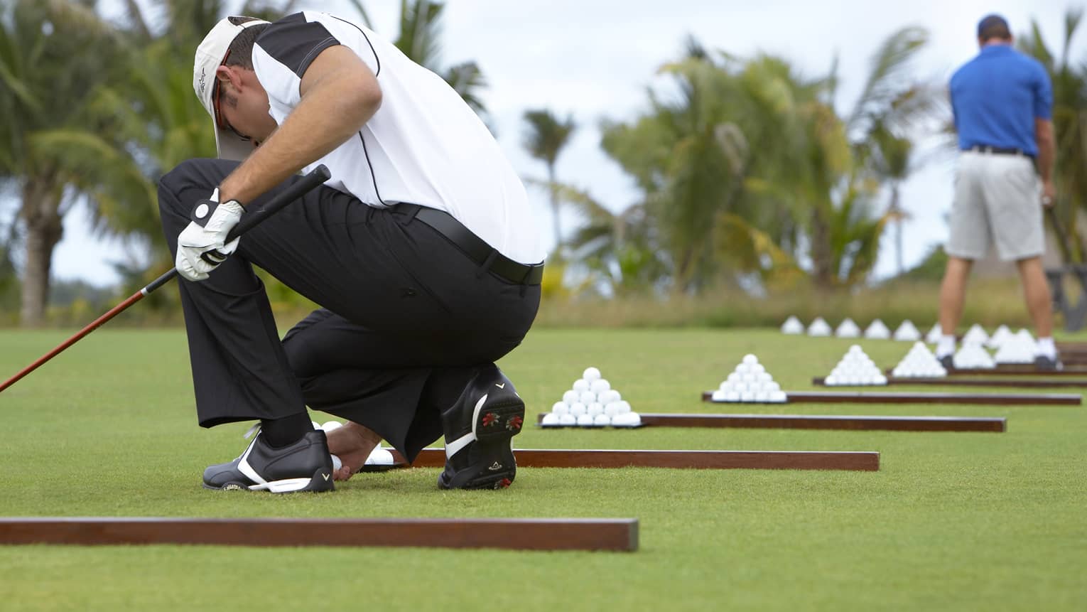 Man holding golf club kneels on driving range