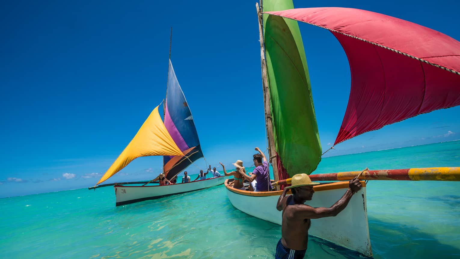 Man in water pulls guests in Mauritian Regatta white boats with colourful sails on lagoon