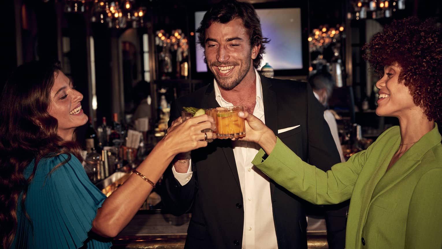 A man and two women toasting with drinks in hand at a bar.