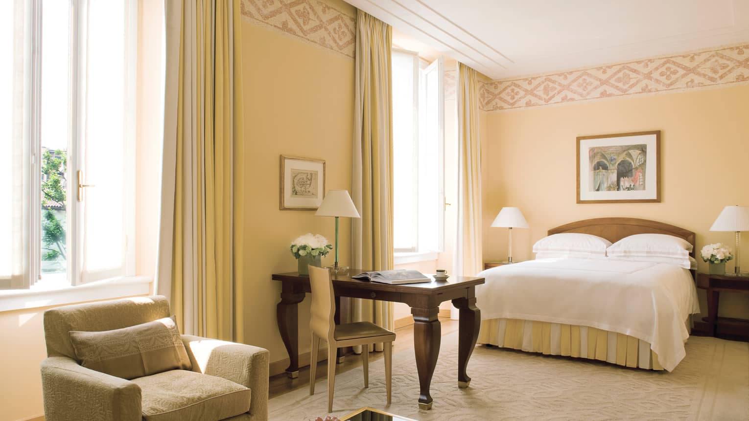 Deluxe Room armchair by table, fruit bowl, wood desk with chair, bed, sunny windows
