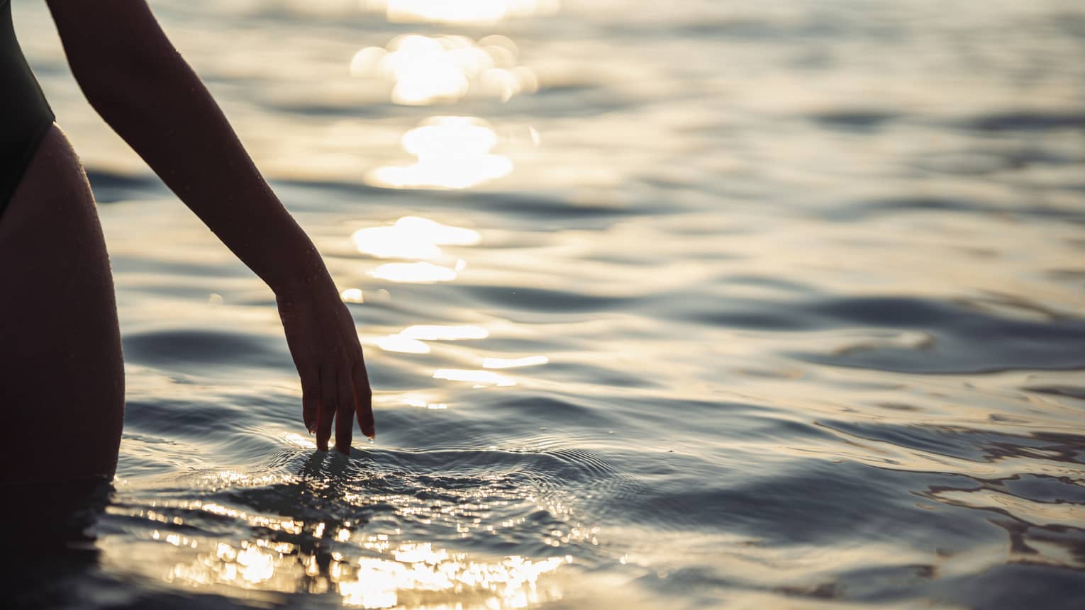 A woman's hand touching ocean water.