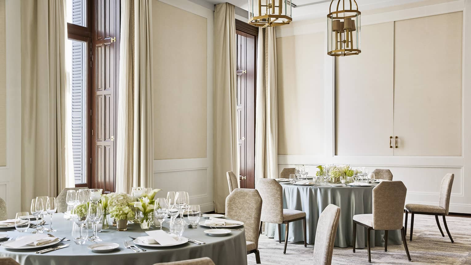 Room with two round banquet tables, each with light green table clothes and six chairs, place settings