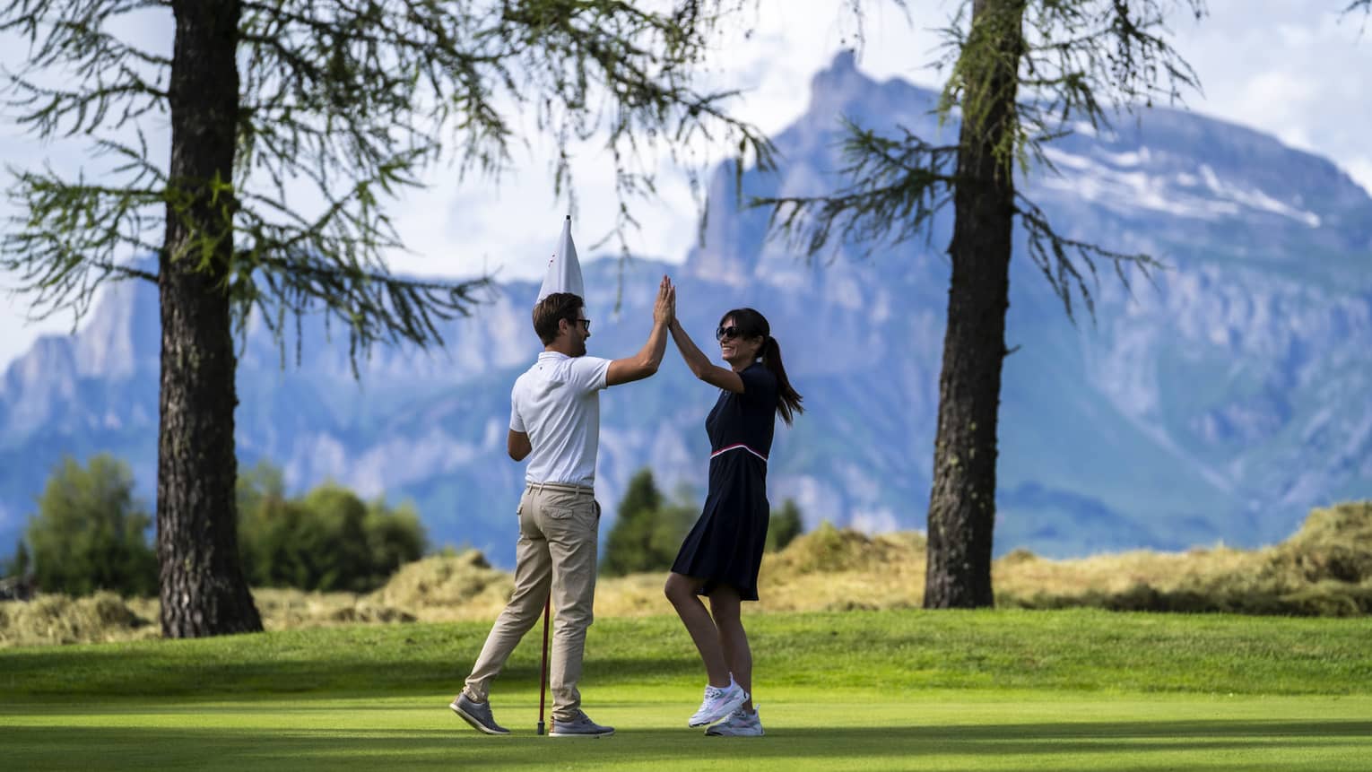 Two people high-fiving on a golf course with mountains in the distance