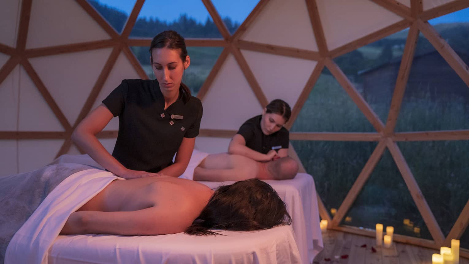Couple lying on spa tables in yurt, receiving massages from spa therapists