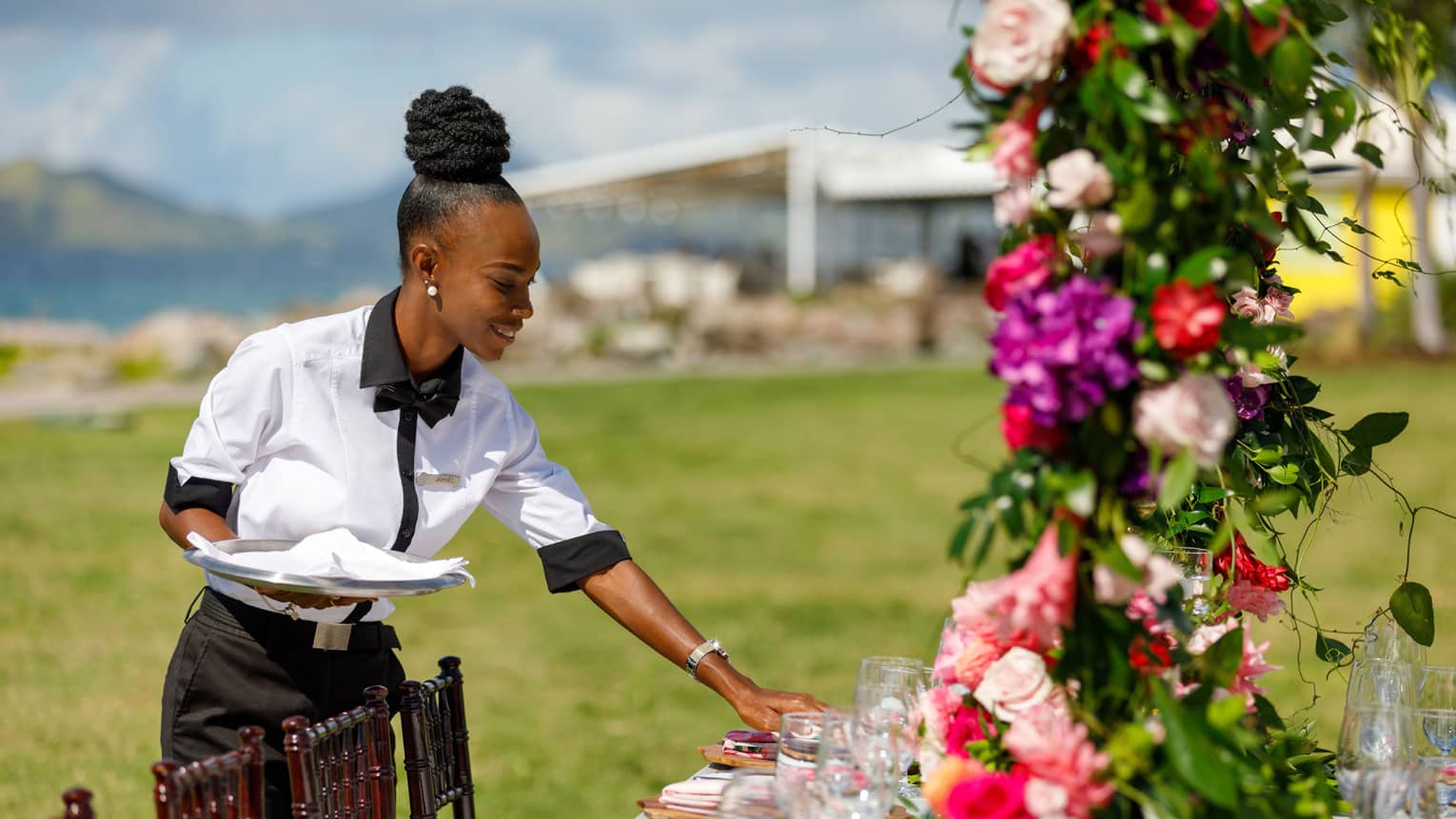 Uniformed wedding service specialist adjusting table setting, pink floral arrangement in forefront