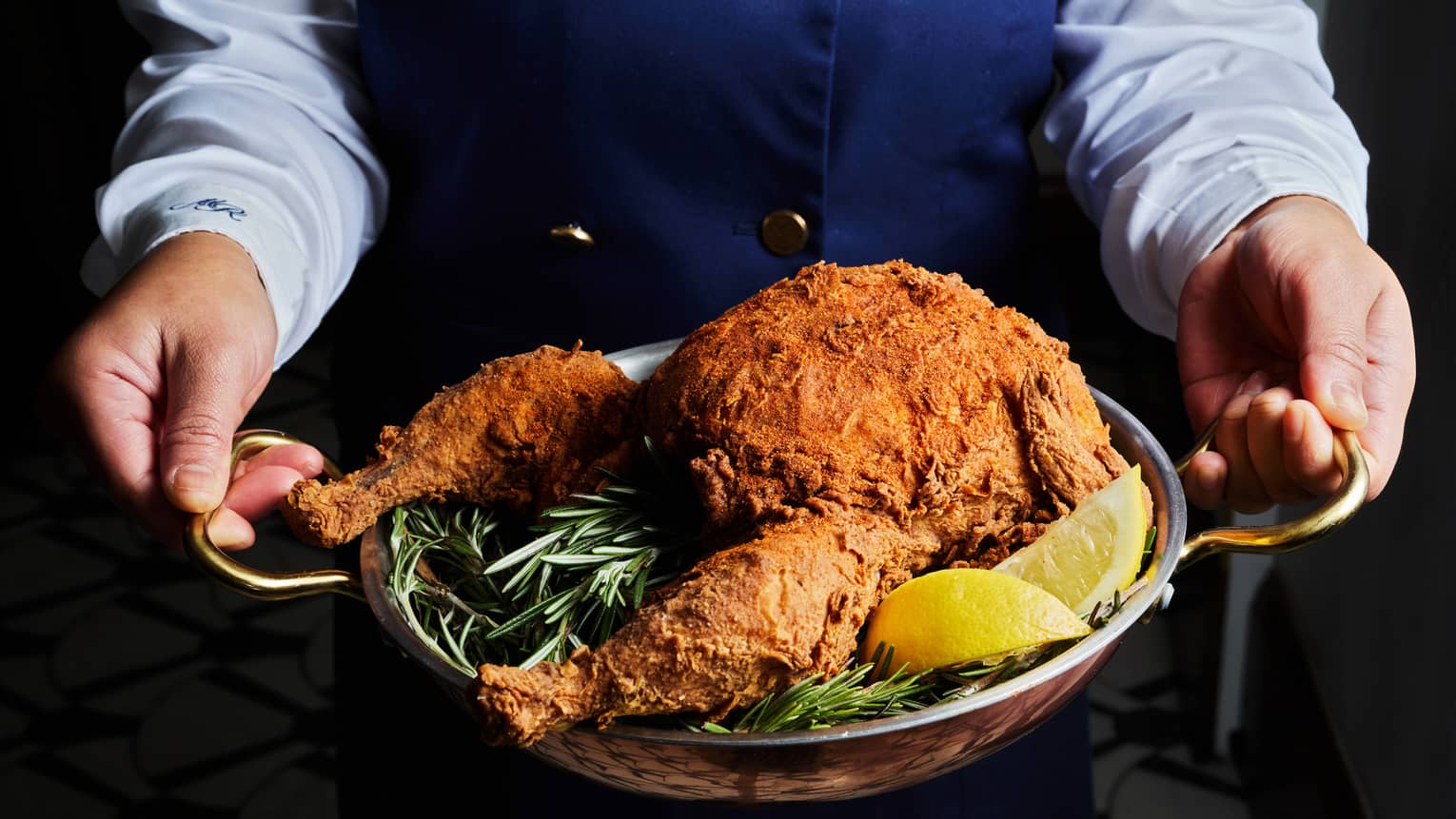 A person holds a serving tray of fried chicken with green garnishes and lemon slides.