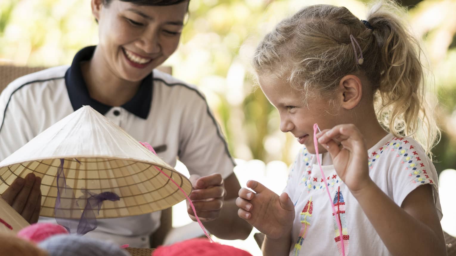 Hotel staff helps young girl thread string on traditional hat
