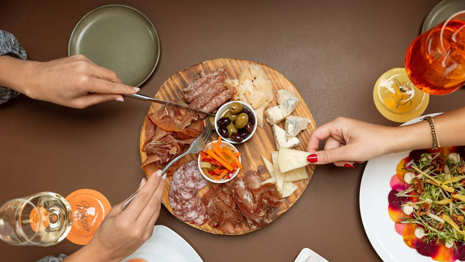 People eating food off of a charcuterie board on a dining table.