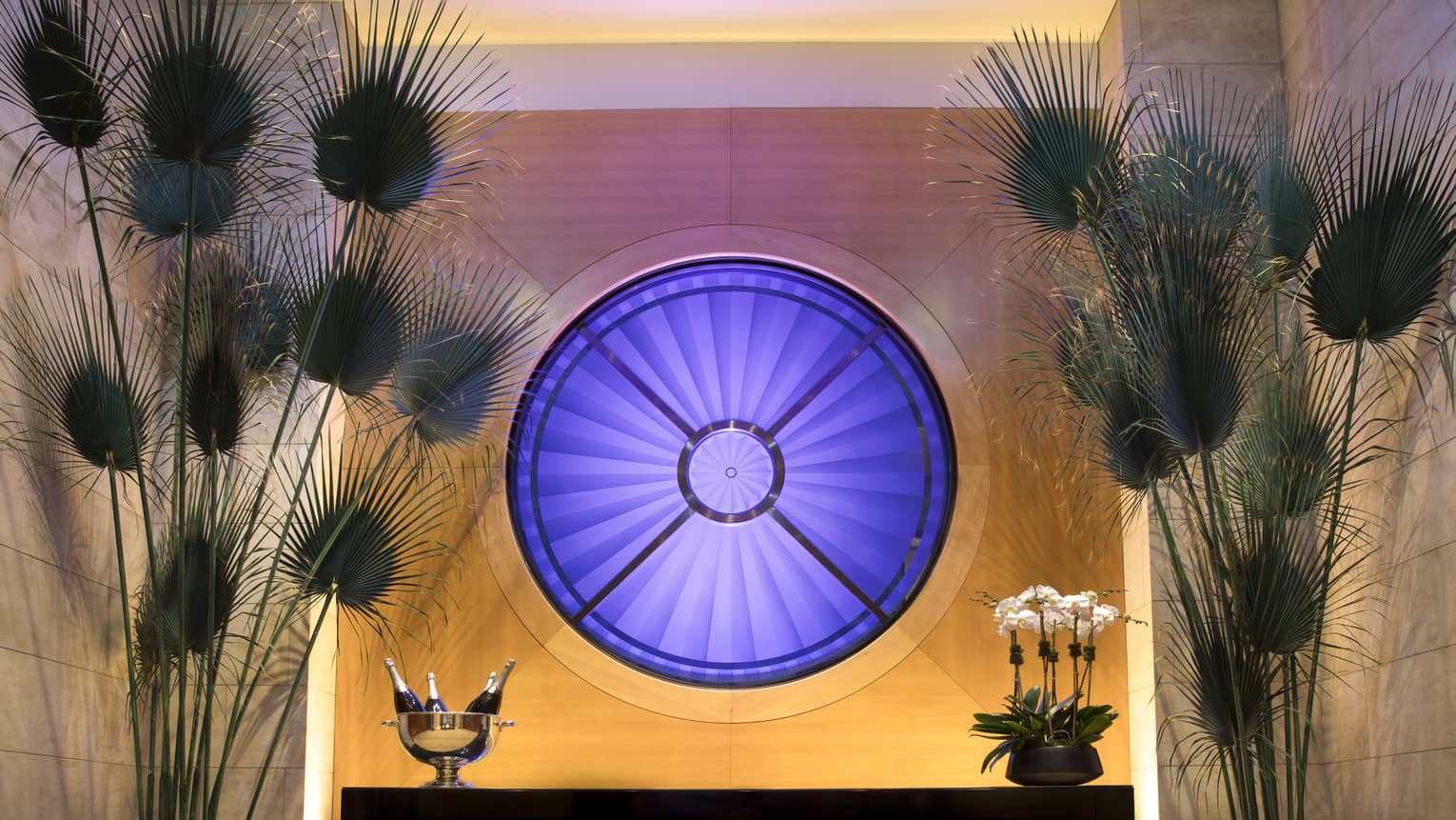 Fifty7 Center round blue Oculus window over buffet table with Champagne, tall fan-shaped tropical plants