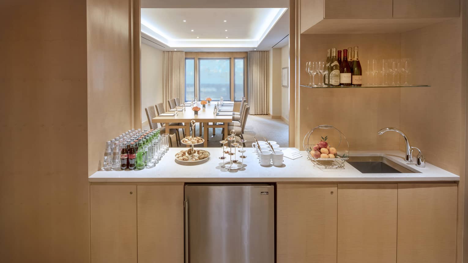 11th Floor Terrace Boardroom pantry with natural wood cabinetry, stainless steel mini fridge, glass shelf holding wine and wine glasses, with a window overlooking the boardroom at four seasons hotel new york