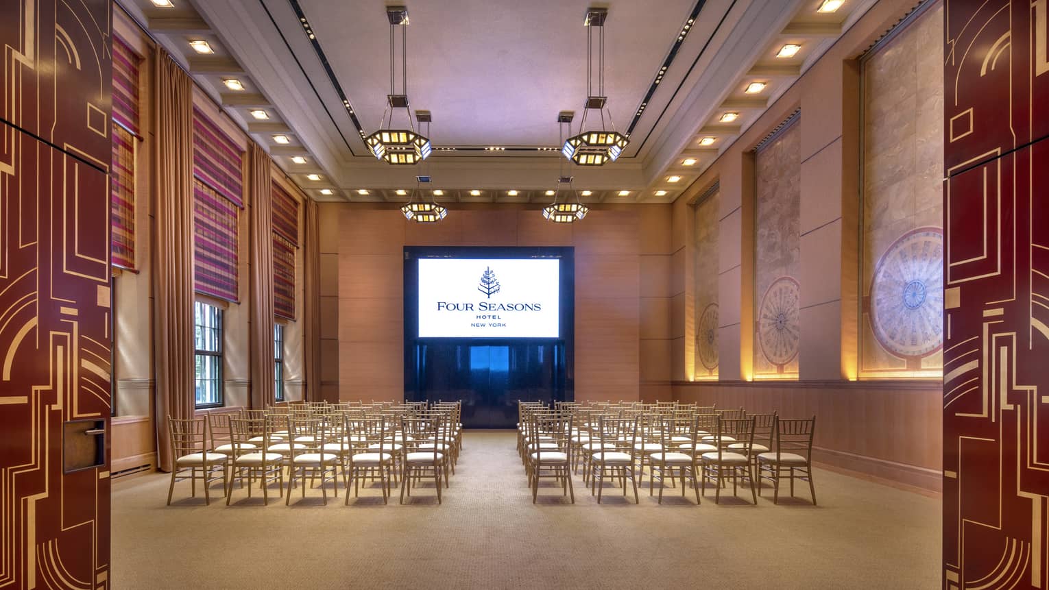 red and gold abstract lines decorate two doors that are opened to reveal a wood-panelled function room with rows of chairs facing a presentation screen