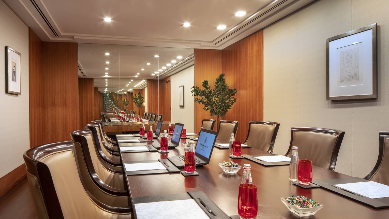 A close up of a long rectangular boardroom table set with a black folder, white paper, pen and clear bottles filled with a red soda. 