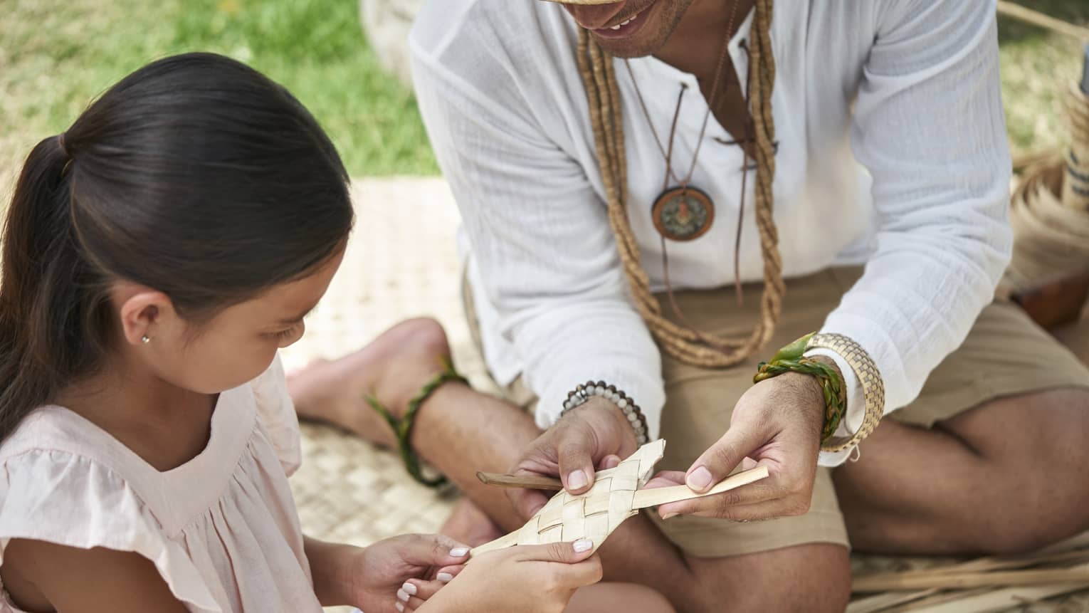 An adult shows a young girl how to weave a basket