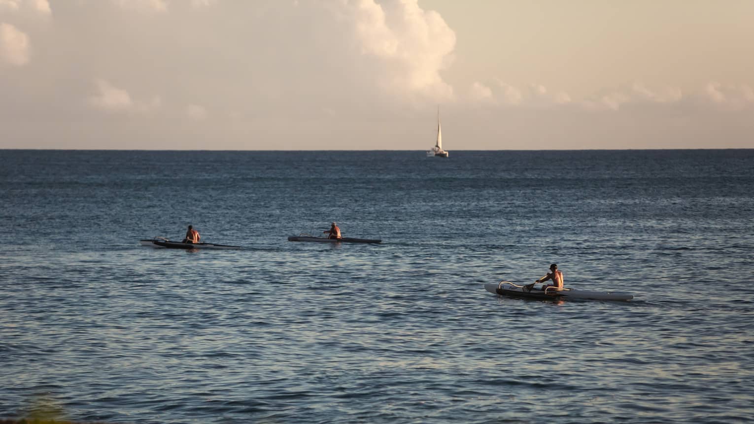 Three kayakers in the ocean with a sailboat in the background