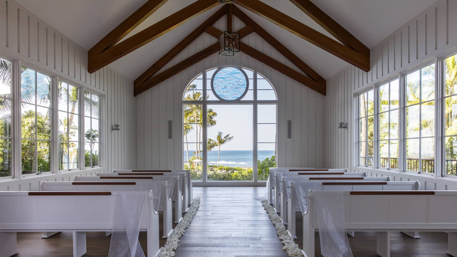 A chapel with white pewes and large windows.