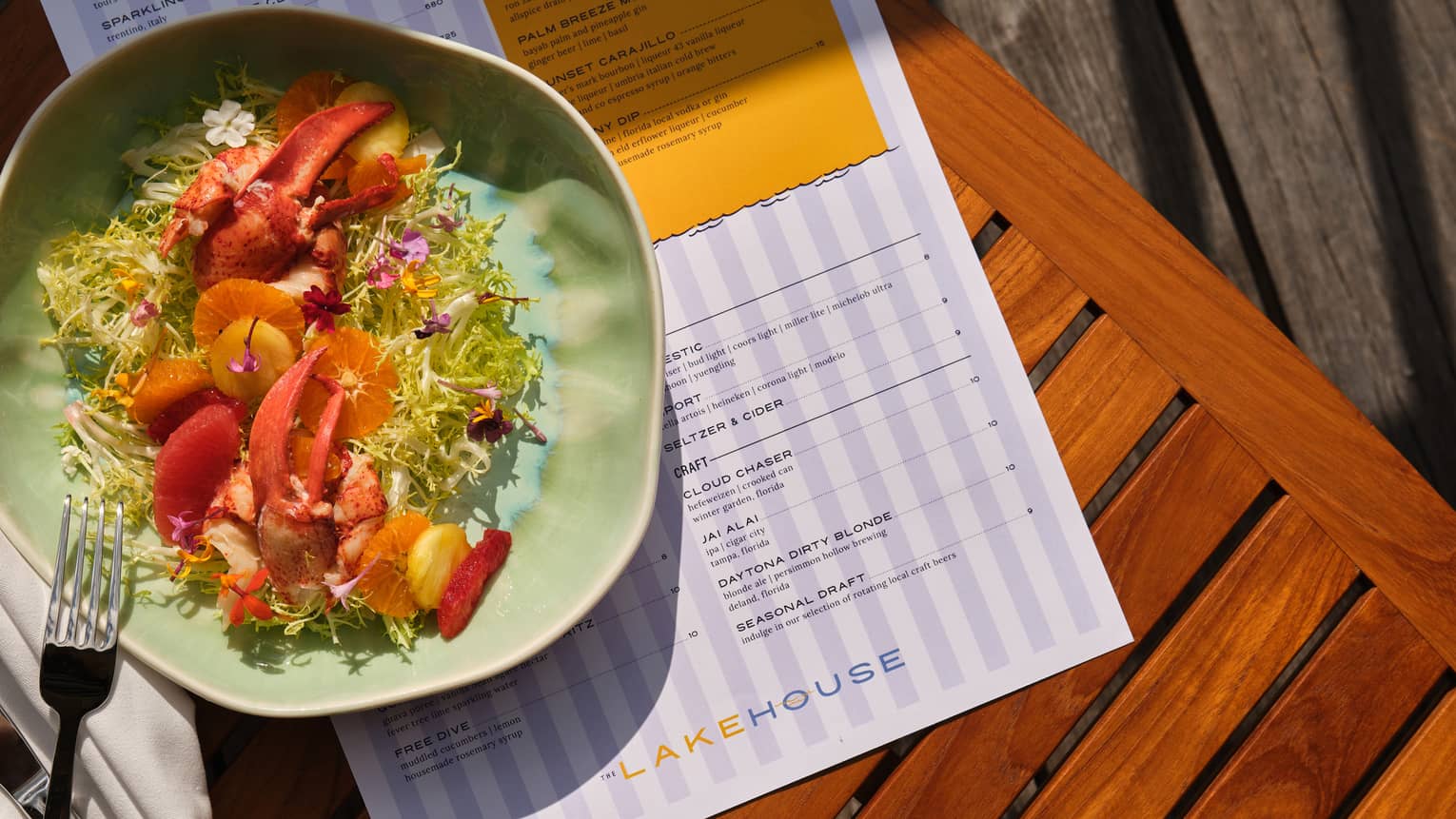 Maine lobster citrus salad with grilled pineapple, blood orange, mint, frisee lettuce and tangerine dressing, served on a green plate on a wood slat table