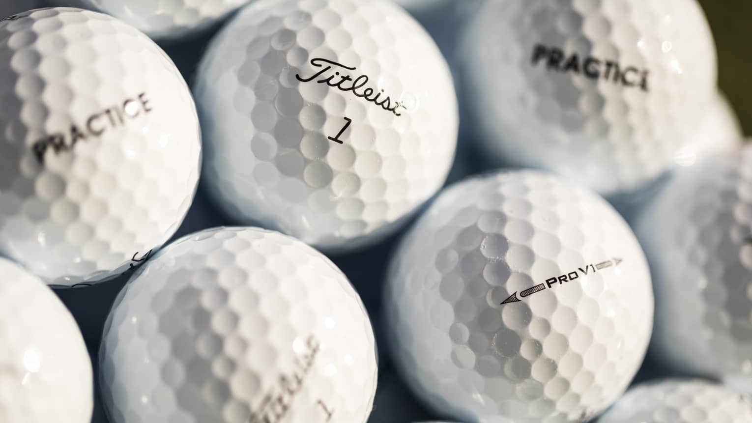 Close-up of white golf balls, each labeled with either Practice, Pro V1, or Titleist 1 in black font.