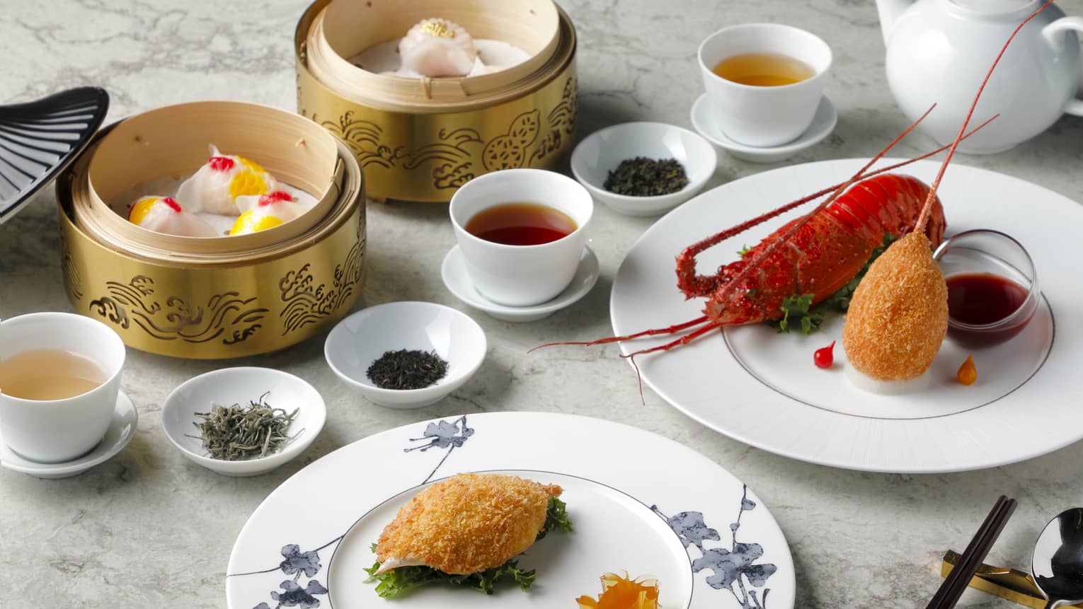 Plain white cups of tea are surrounded by bowls of dried tea leaves, baskets of dumplings and plates of lobster and seafood.