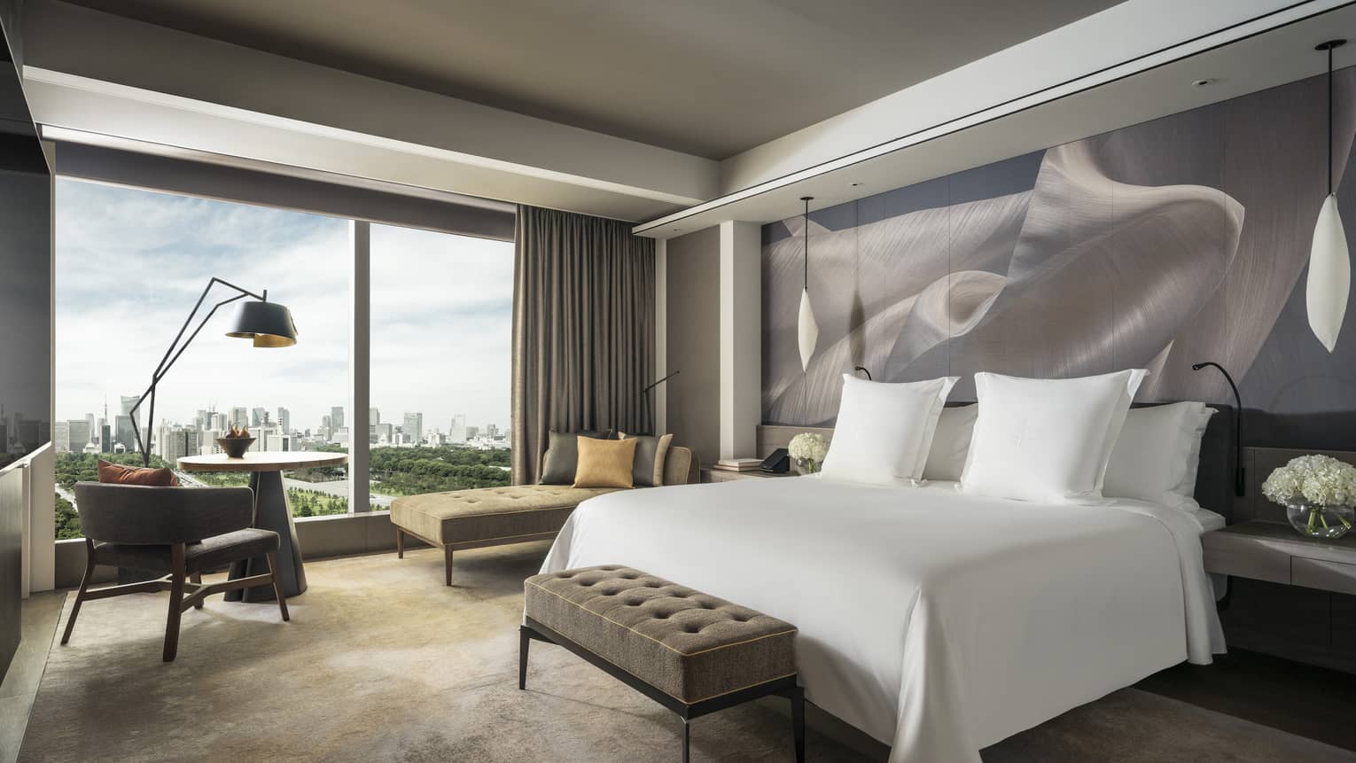 Hotel room with a cushioned bench at the end of white king bed and a wall of windows