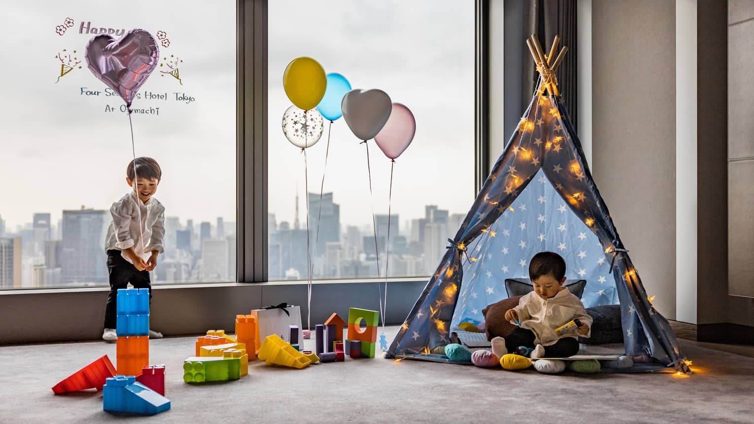 Two children play amid toy building blocks, helium balloons and a tent in a guest room at Four Seasons Hotel Tokyo at Otemachi