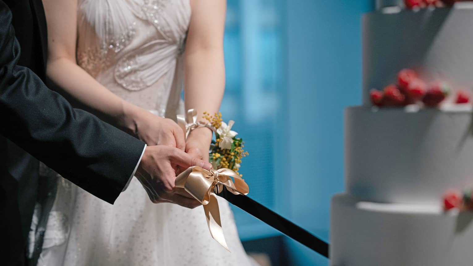 Hands of bride and groom cut a tiered wedding cake